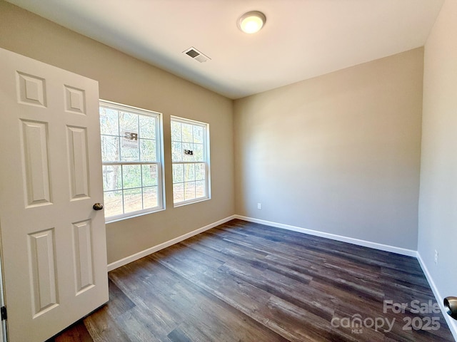 empty room with baseboards, visible vents, and dark wood-type flooring