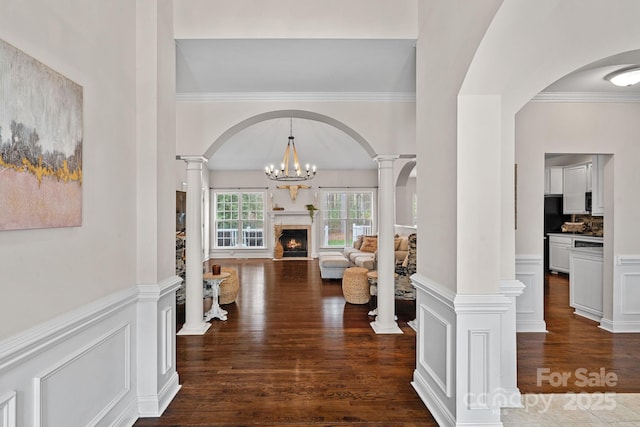 foyer entrance with arched walkways, wood finished floors, decorative columns, ornamental molding, and a fireplace with flush hearth