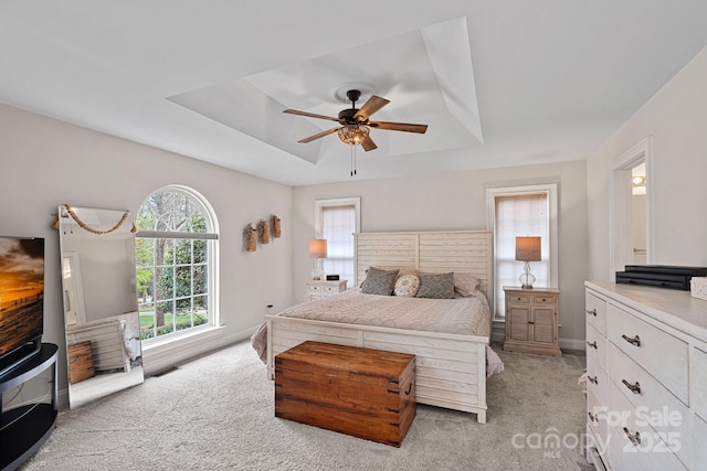 bedroom featuring a ceiling fan, baseboards, light colored carpet, and a tray ceiling