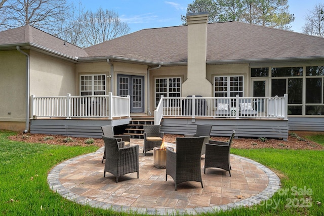 back of house featuring a deck, a patio area, a chimney, roof with shingles, and an outdoor fire pit