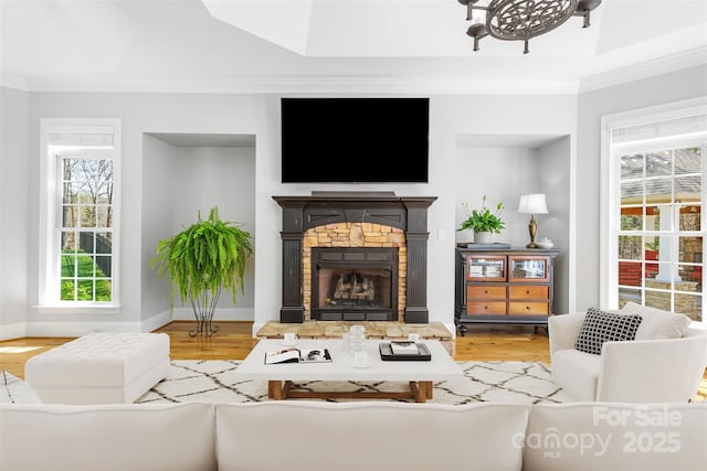 living room featuring a healthy amount of sunlight, a fireplace, ornamental molding, and wood finished floors