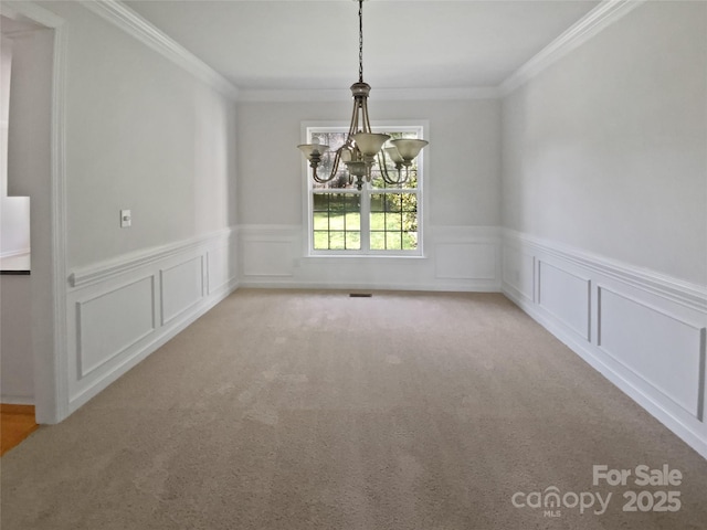 unfurnished dining area with wainscoting, ornamental molding, a notable chandelier, and light colored carpet