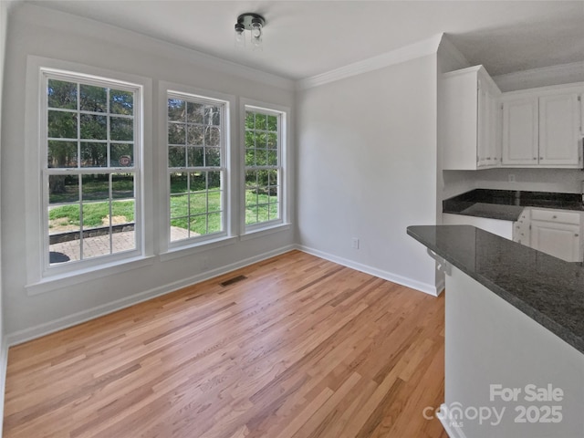unfurnished dining area featuring light wood finished floors, baseboards, visible vents, and ornamental molding