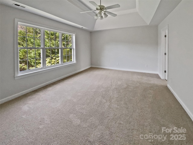 carpeted spare room featuring a tray ceiling, baseboards, visible vents, and ceiling fan