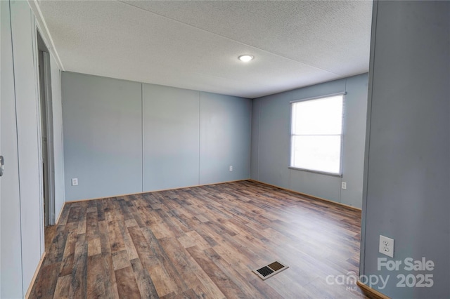 spare room featuring visible vents, wood finished floors, and a textured ceiling