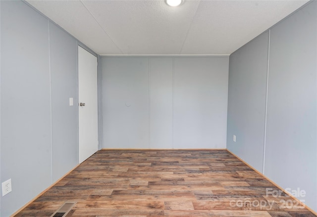 empty room featuring a decorative wall, wood finished floors, a textured ceiling, and visible vents