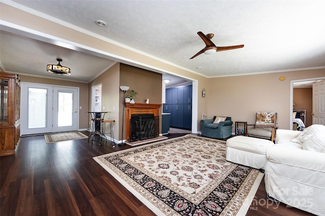 living area featuring baseboards, a ceiling fan, crown molding, a fireplace with raised hearth, and wood finished floors