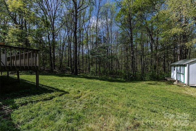 view of yard with a shed, a deck, a view of trees, and an outbuilding