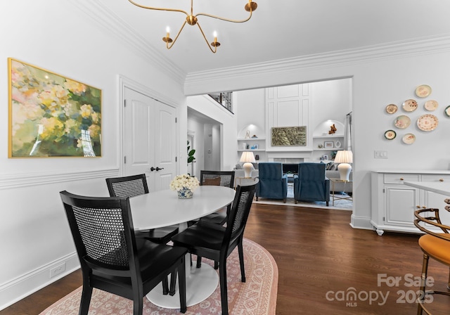 dining area featuring crown molding, a fireplace, a chandelier, built in shelves, and dark wood finished floors