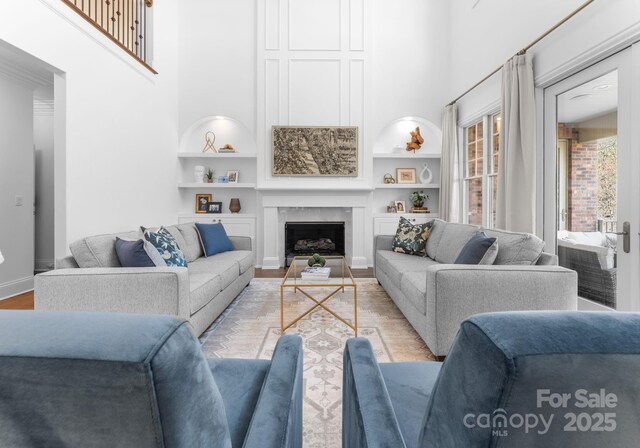 living area with light wood finished floors, a fireplace, a high ceiling, and built in shelves