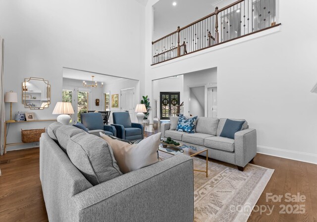 living area with an inviting chandelier, baseboards, a high ceiling, and wood finished floors