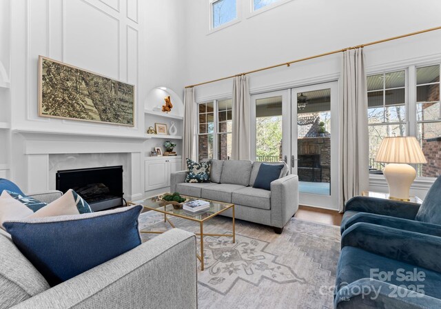 living area with a towering ceiling, wood finished floors, a high end fireplace, built in shelves, and french doors