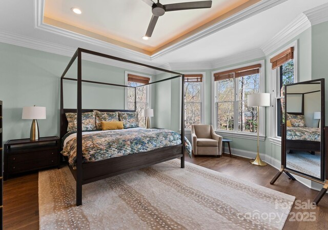 bedroom with wood finished floors, baseboards, ornamental molding, a tray ceiling, and recessed lighting