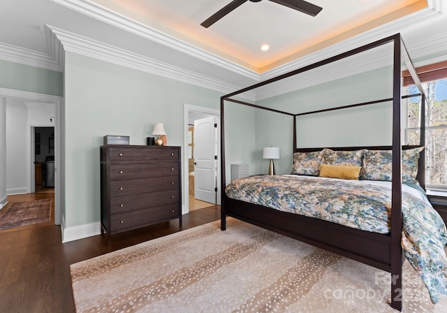 bedroom featuring baseboards, ornamental molding, a raised ceiling, and wood finished floors