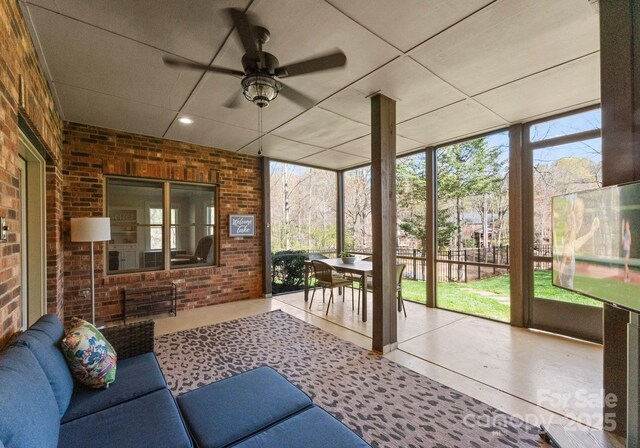 sunroom / solarium featuring a ceiling fan, brick wall, floor to ceiling windows, and a wealth of natural light