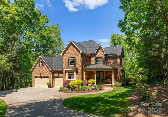 traditional-style home with roof with shingles, brick siding, a porch, a front yard, and driveway