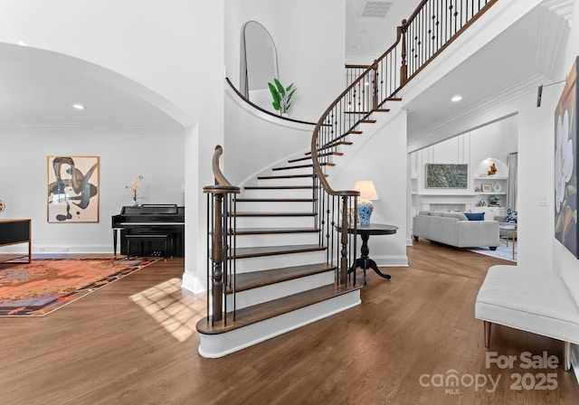 stairs featuring visible vents, arched walkways, a high ceiling, and wood finished floors