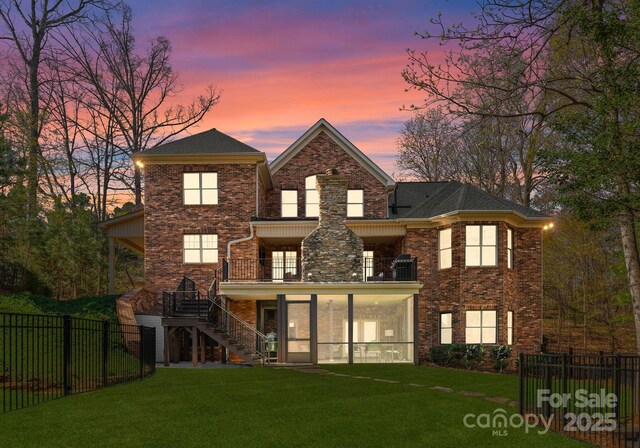 exterior space featuring a balcony, a fenced backyard, brick siding, a lawn, and stairway