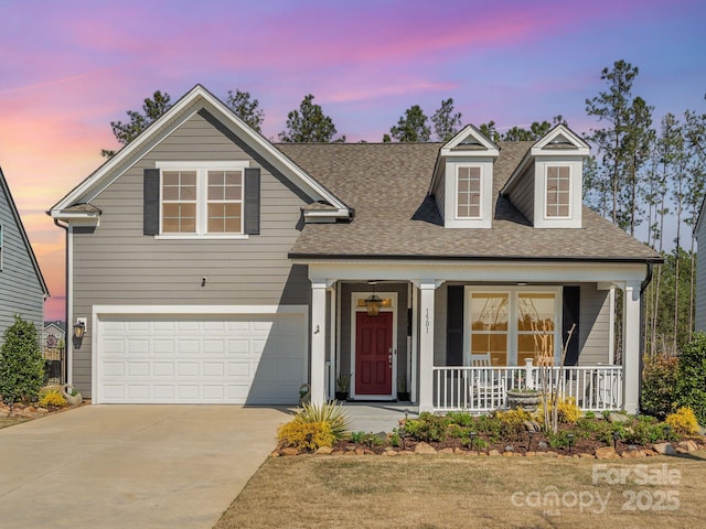 traditional-style home with a shingled roof, an attached garage, a porch, and concrete driveway