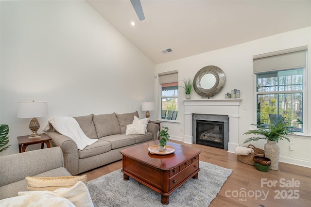 living room featuring visible vents, a glass covered fireplace, a ceiling fan, and wood finished floors