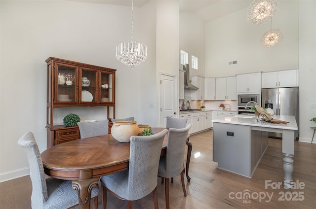 dining area with baseboards, light wood-type flooring, a high ceiling, and a chandelier