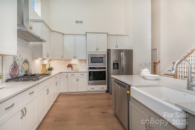 kitchen featuring visible vents, a towering ceiling, wall chimney exhaust hood, stainless steel appliances, and a sink