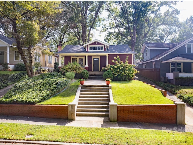 bungalow-style home with central air condition unit, stairway, and a front yard