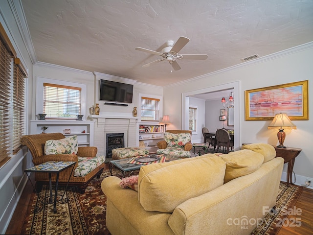 living room featuring ornamental molding, visible vents, a ceiling fan, a fireplace, and wood finished floors