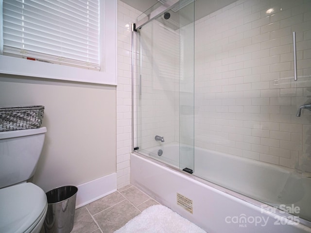 bathroom featuring baseboards, toilet, shower / bath combination with glass door, and tile patterned floors