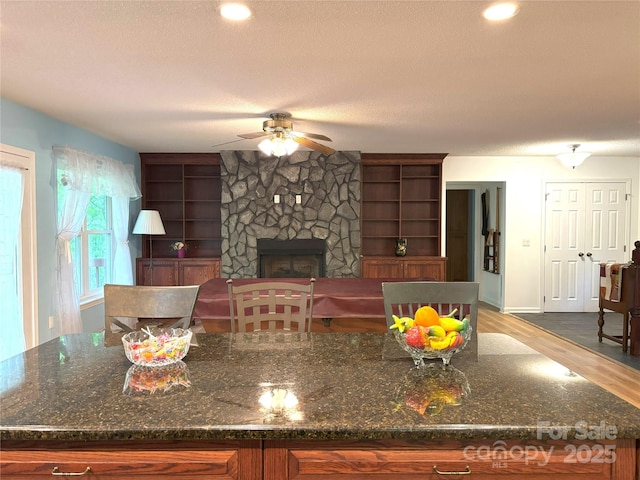 97 Hughes Dr, Maggie Valley, NC 28751 - kitchen with ceiling fan, wood finished floors, a fireplace, a textured ceiling, and dark stone counters