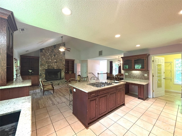 97 Hughes Dr, Maggie Valley, NC 28751 - kitchen featuring a stone fireplace, ceiling fan, stainless steel gas cooktop, light tile patterned floors, and plenty of natural light