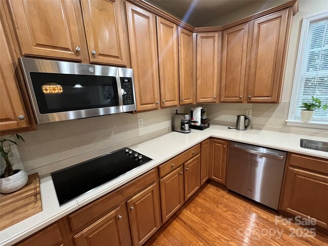 7925 Woodmere Dr, Harrisburg, NC 28075 - kitchen with stainless steel appliances, light wood-type flooring, light countertops, and brown cabinetry