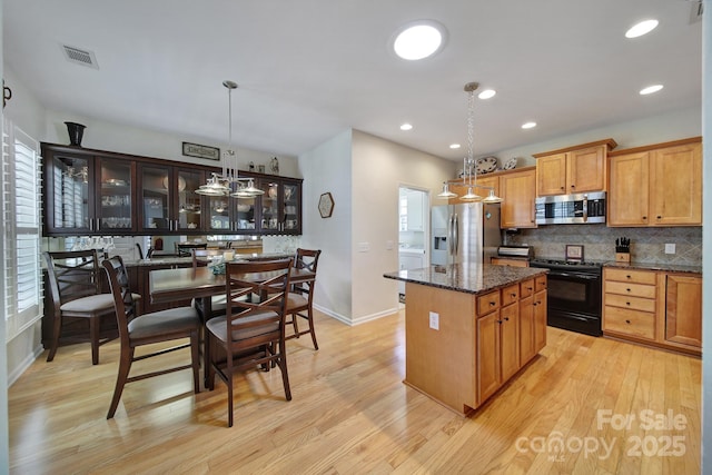 kitchen with light wood-type flooring, decorative backsplash, a kitchen island, visible vents, and appliances with stainless steel finishes