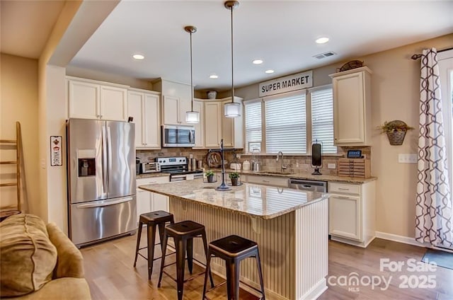 kitchen with backsplash, light wood-style flooring, appliances with stainless steel finishes, and a breakfast bar area