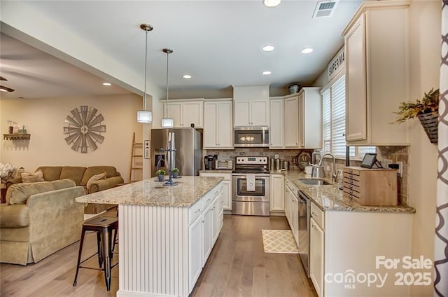 kitchen featuring a sink, open floor plan, stainless steel appliances, a kitchen bar, and visible vents