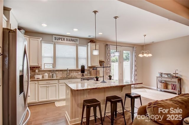 kitchen featuring a sink, a breakfast bar area, stainless steel fridge with ice dispenser, white cabinetry, and light stone countertops