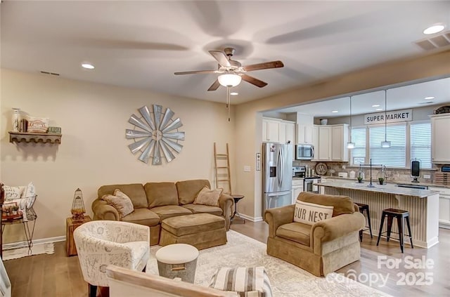living area featuring light wood-type flooring, visible vents, a ceiling fan, and baseboards