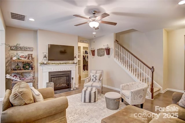 living area with stairway, visible vents, wood finished floors, and ceiling fan