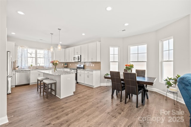 kitchen featuring stainless steel appliances, a sink, a kitchen island, recessed lighting, and white cabinets
