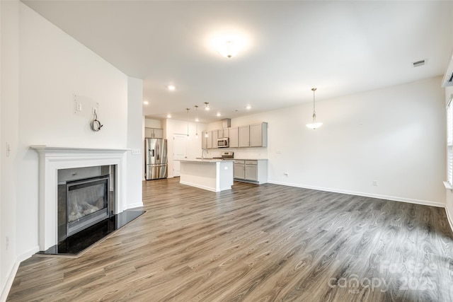 unfurnished living room featuring recessed lighting, baseboards, a glass covered fireplace, and wood finished floors
