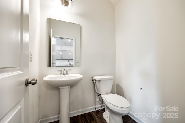 half bath with toilet, wood finished floors, baseboards, and a sink