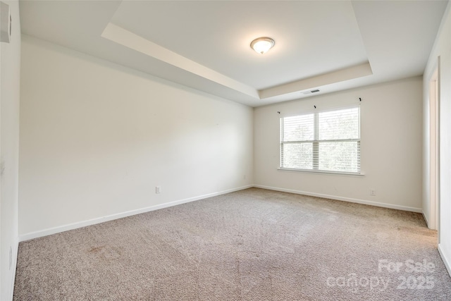 carpeted spare room with baseboards, a raised ceiling, and visible vents