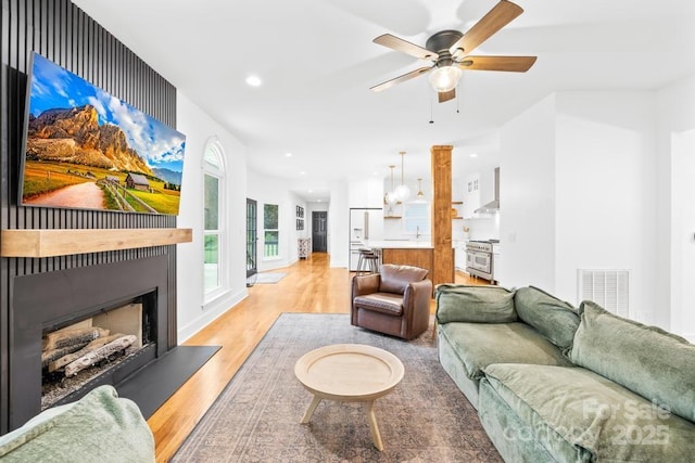 living area with recessed lighting, a fireplace with raised hearth, light wood finished floors, visible vents, and a ceiling fan