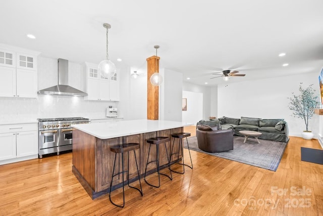 kitchen with recessed lighting, wall chimney exhaust hood, a kitchen breakfast bar, and range with two ovens