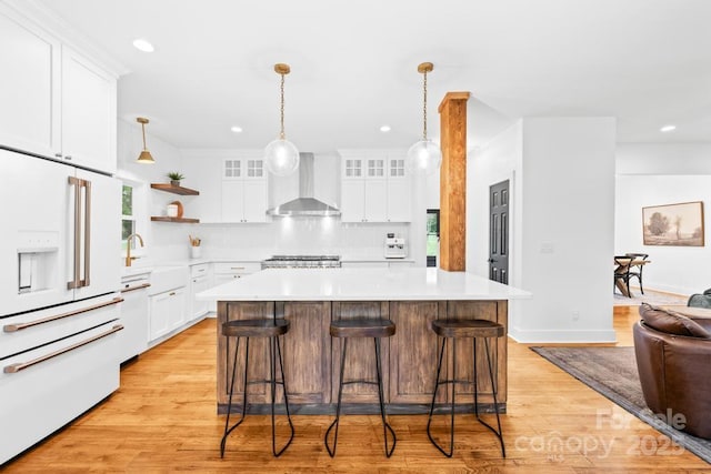 kitchen with a sink, white appliances, glass insert cabinets, light countertops, and wall chimney exhaust hood