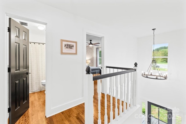 hallway featuring a notable chandelier, wood finished floors, an upstairs landing, and visible vents