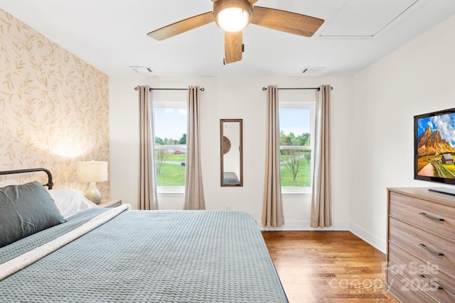 bedroom featuring wood finished floors, wallpapered walls, attic access, baseboards, and visible vents