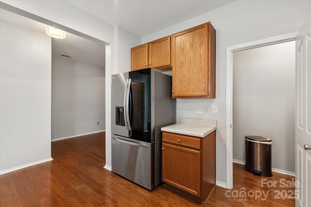 kitchen featuring wood finished floors, brown cabinetry, stainless steel fridge with ice dispenser, light countertops, and baseboards