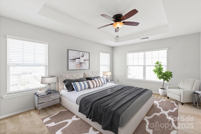 bedroom with a raised ceiling, visible vents, baseboards, and multiple windows