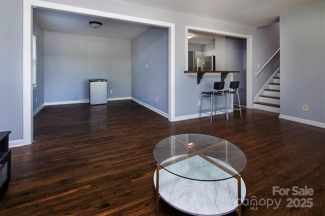 unfurnished living room featuring baseboards, wood finished floors, and stairs